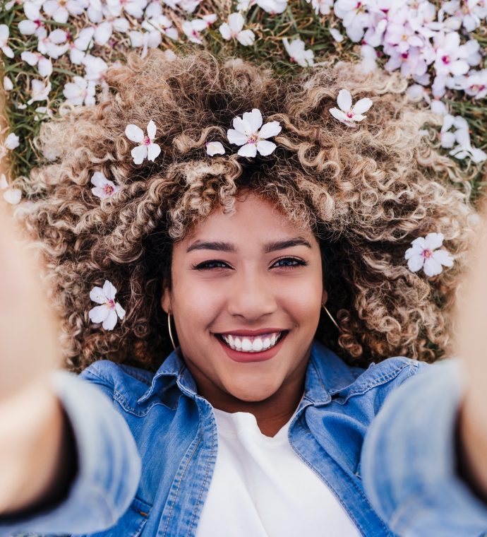 top view of happy hispanic woman with afro hair lying on grass among pink blossom flowers.Springtime