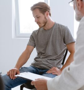 Young handsome problematic patient during counseling with grey senior therapist